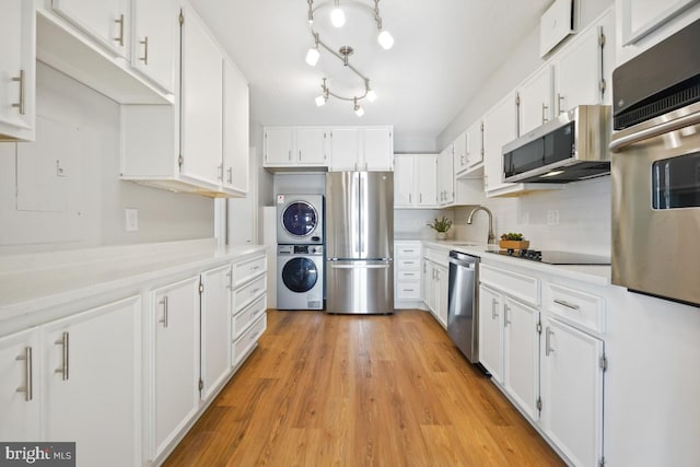 kitchen featuring white cabinetry, sink, light hardwood / wood-style flooring, stacked washer / drying machine, and appliances with stainless steel finishes