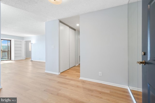 spare room featuring built in shelves, light hardwood / wood-style floors, and a textured ceiling