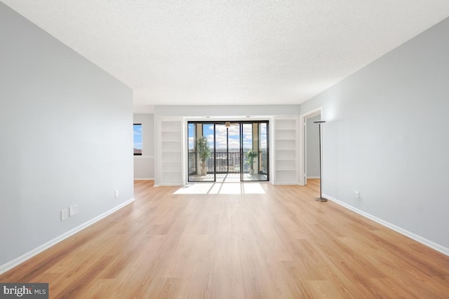 unfurnished living room with built in features, light hardwood / wood-style flooring, and a textured ceiling