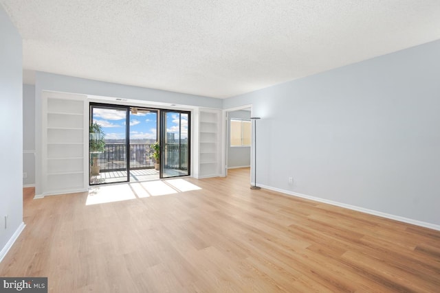 unfurnished room featuring built in shelves, a textured ceiling, and light hardwood / wood-style flooring