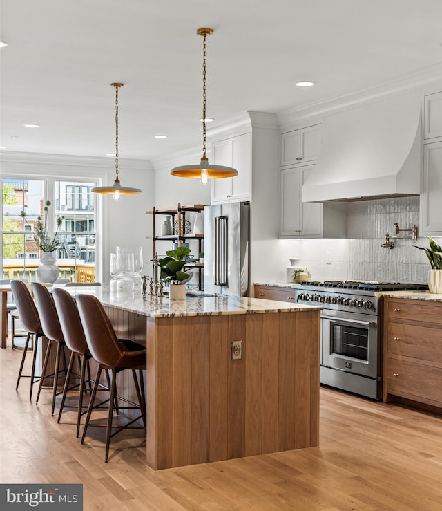 kitchen featuring light wood-type flooring, light stone counters, custom exhaust hood, white cabinetry, and premium appliances