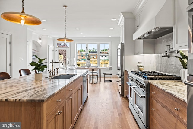 kitchen featuring custom range hood, stainless steel appliances, white cabinetry, an island with sink, and pendant lighting