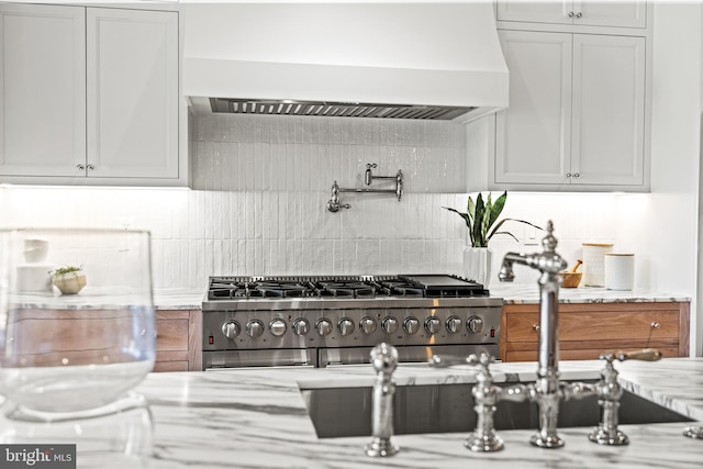 kitchen with custom exhaust hood, light stone countertops, backsplash, and white cabinetry