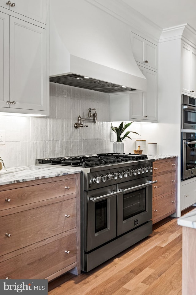 kitchen featuring custom range hood, light hardwood / wood-style floors, crown molding, stainless steel appliances, and white cabinets