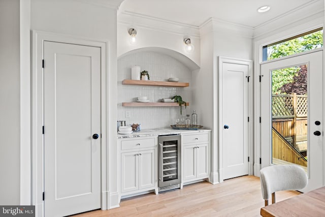 bar with light wood-type flooring, crown molding, wine cooler, and white cabinets