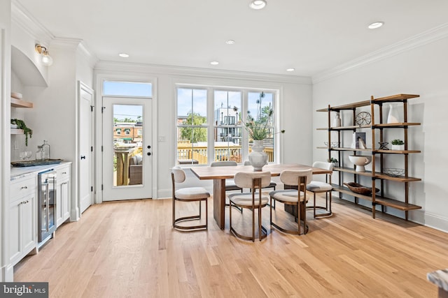 dining area featuring beverage cooler, light hardwood / wood-style floors, and ornamental molding