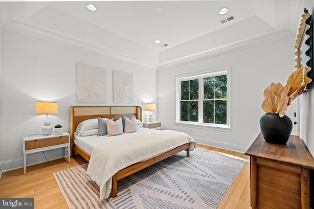 bedroom featuring a tray ceiling, light hardwood / wood-style floors, and ornamental molding