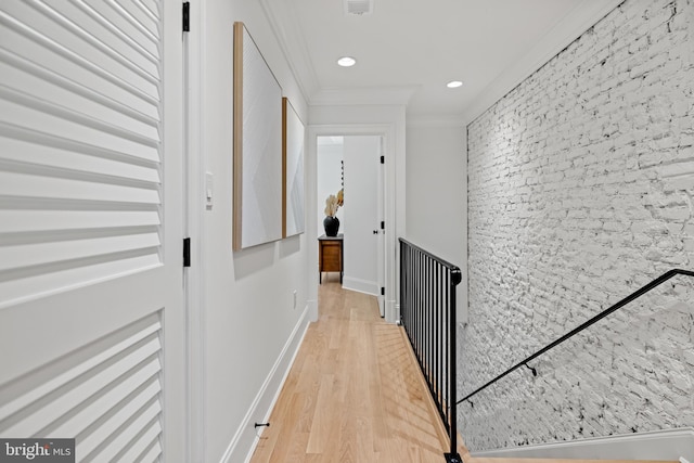 corridor with crown molding, light wood-type flooring, and brick wall