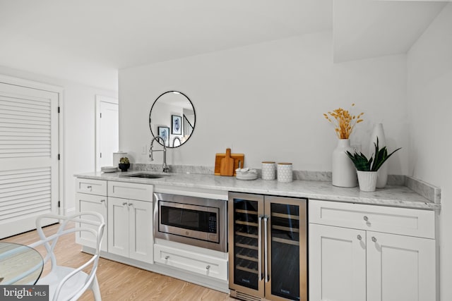 bar with light hardwood / wood-style floors, white cabinetry, sink, beverage cooler, and stainless steel microwave