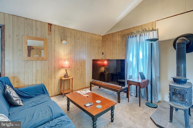 living room featuring a wood stove, vaulted ceiling, carpet floors, and wooden walls