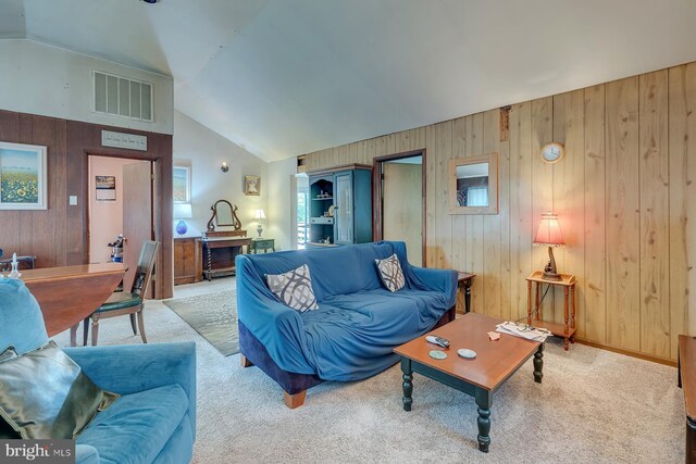 carpeted living room featuring vaulted ceiling and wood walls