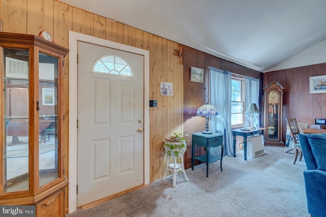 foyer entrance with lofted ceiling, plenty of natural light, carpet, and wooden walls