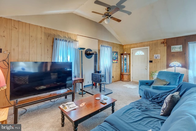 living room featuring carpet flooring, a wood stove, lofted ceiling, wood walls, and ceiling fan