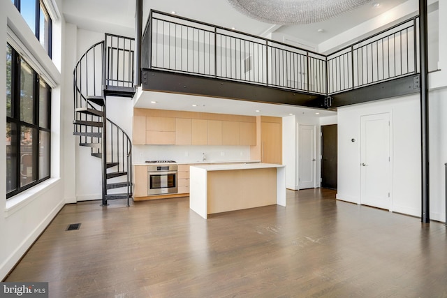 kitchen with a center island, appliances with stainless steel finishes, light brown cabinets, dark hardwood / wood-style floors, and a high ceiling