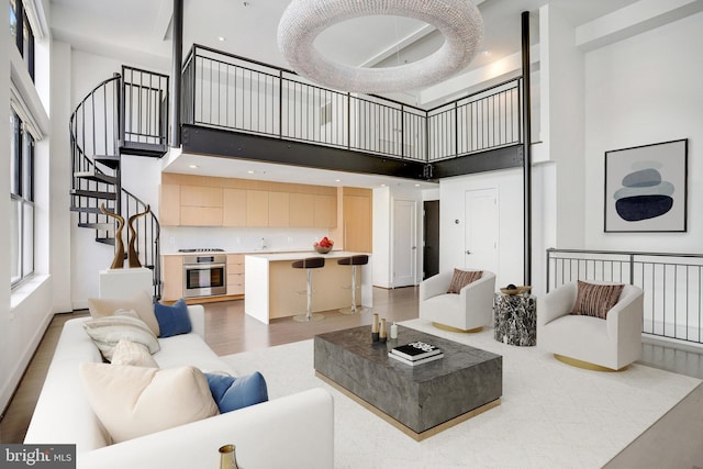 living area featuring stairway, baseboards, light wood-type flooring, and a towering ceiling