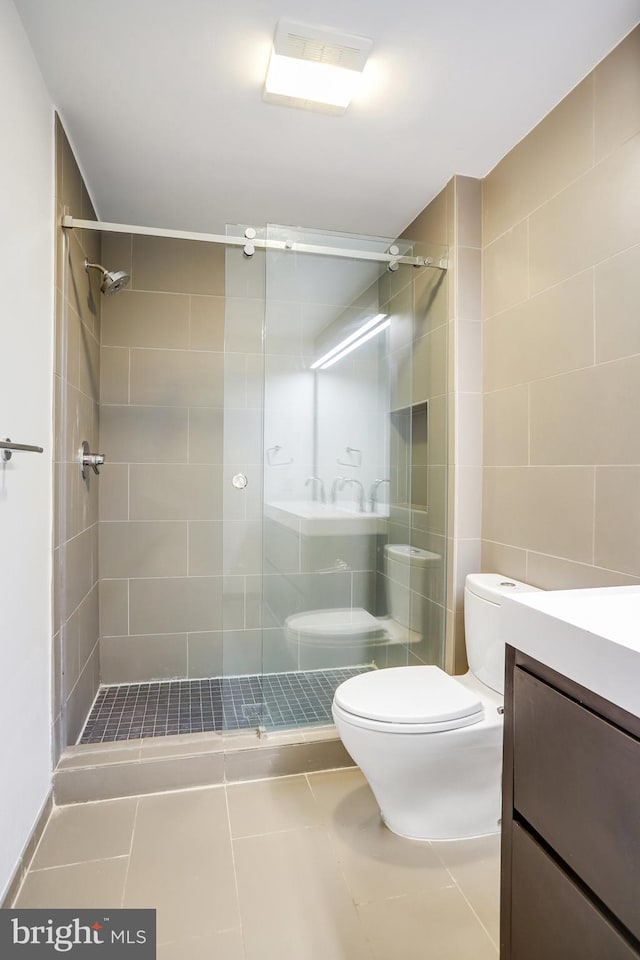 bathroom with tile patterned flooring, toilet, a tile shower, and vanity