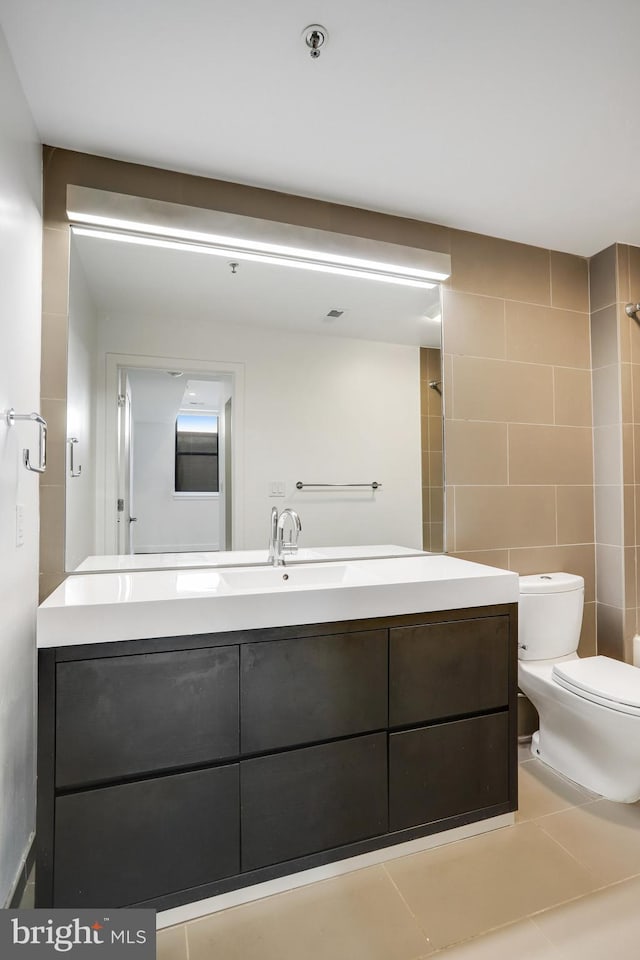 bathroom featuring tile patterned flooring, toilet, tile walls, a shower with shower door, and vanity