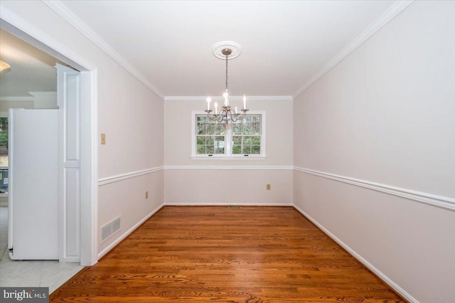 unfurnished dining area featuring crown molding, hardwood / wood-style flooring, and an inviting chandelier