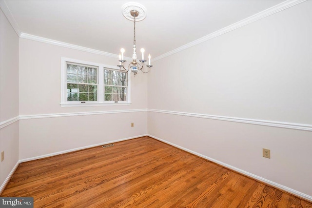 empty room with hardwood / wood-style flooring, crown molding, and a notable chandelier