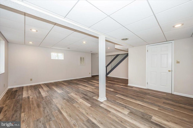 basement featuring a paneled ceiling and dark hardwood / wood-style flooring