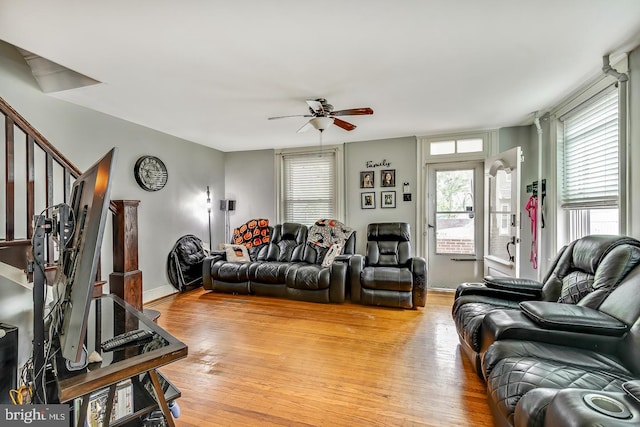 living room featuring ceiling fan, light wood finished floors, stairway, and baseboards