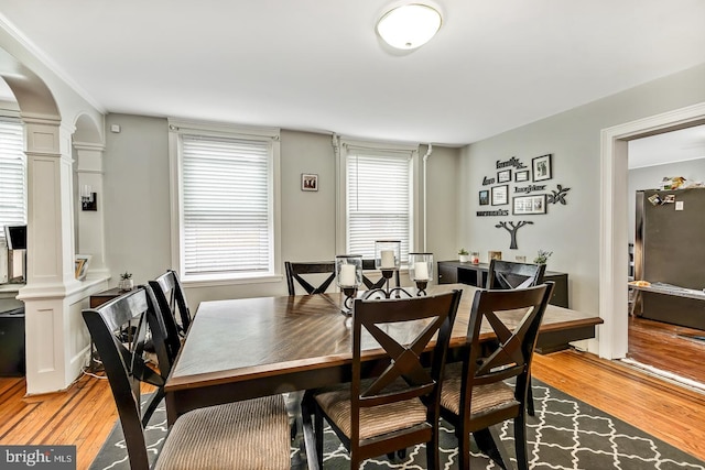 dining space featuring light wood-type flooring, ornate columns, and arched walkways