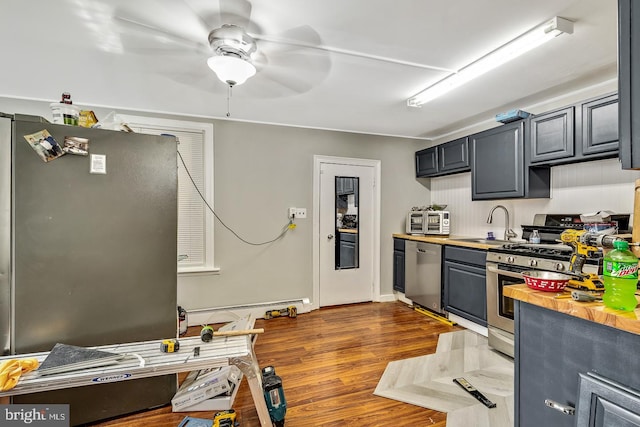 kitchen with dark wood-style flooring, butcher block counters, appliances with stainless steel finishes, a sink, and ceiling fan