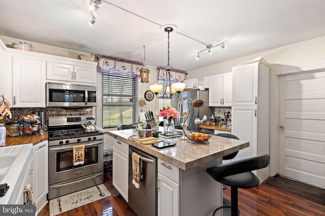 kitchen with dark wood-type flooring, stainless steel appliances, white cabinets, and a kitchen island