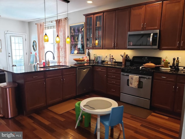 kitchen with pendant lighting, appliances with stainless steel finishes, dark wood-type flooring, kitchen peninsula, and sink