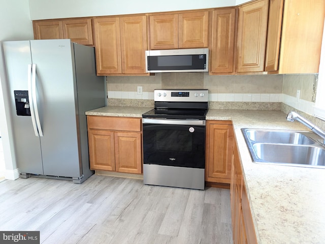 kitchen with stainless steel appliances, sink, tasteful backsplash, and light hardwood / wood-style floors