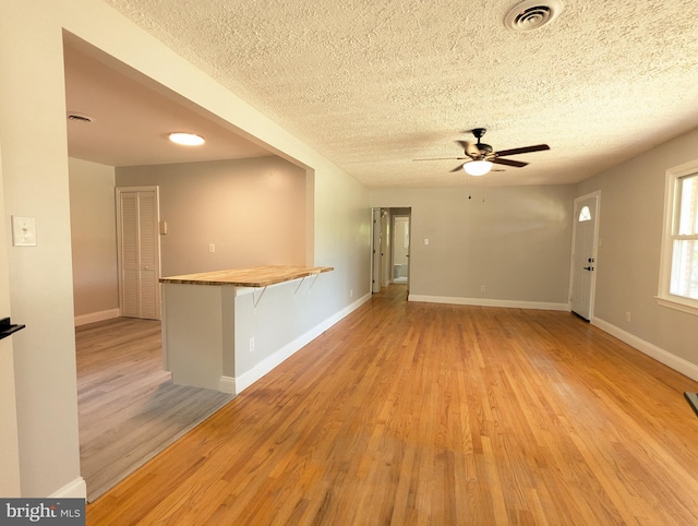 empty room with a textured ceiling, ceiling fan, and light hardwood / wood-style floors