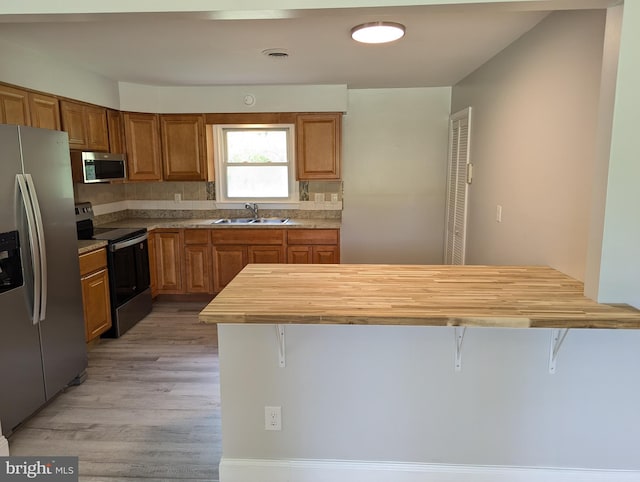 kitchen featuring appliances with stainless steel finishes, a kitchen breakfast bar, backsplash, and light hardwood / wood-style flooring