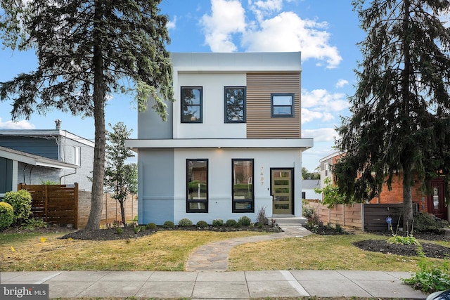 contemporary home with a front yard, fence, and stucco siding