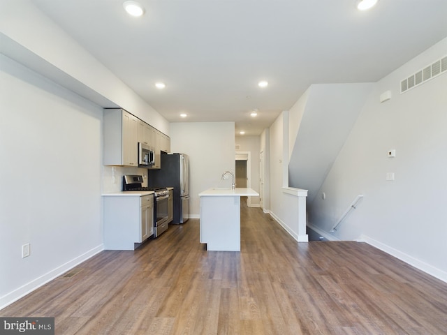 kitchen with decorative backsplash, wood-type flooring, a center island with sink, sink, and stainless steel appliances