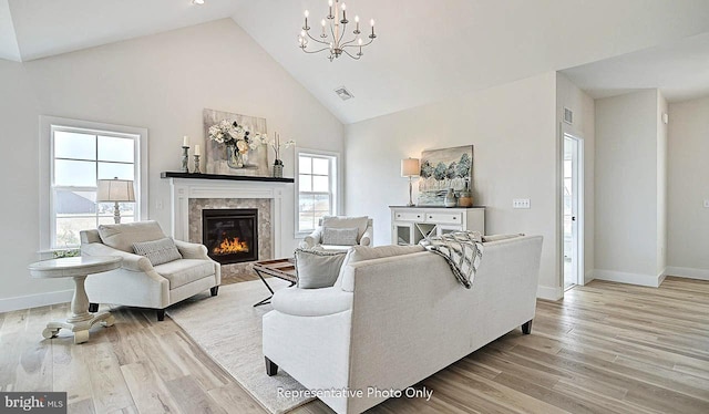 living room with a fireplace, light wood-type flooring, high vaulted ceiling, and a chandelier