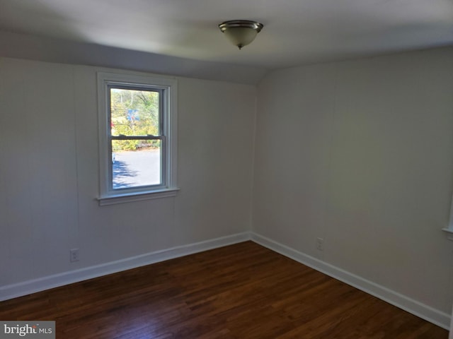 spare room featuring dark wood-type flooring and vaulted ceiling