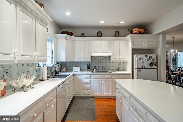 kitchen featuring white appliances, tasteful backsplash, under cabinet range hood, white cabinetry, and a sink