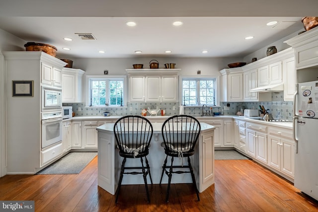 kitchen featuring white appliances, a kitchen island, a sink, visible vents, and a kitchen breakfast bar