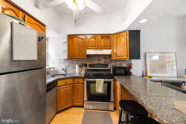 kitchen featuring ceiling fan, sink, light hardwood / wood-style flooring, stainless steel appliances, and dark stone counters