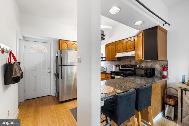 kitchen featuring tasteful backsplash, light hardwood / wood-style flooring, appliances with stainless steel finishes, a breakfast bar area, and dark stone counters