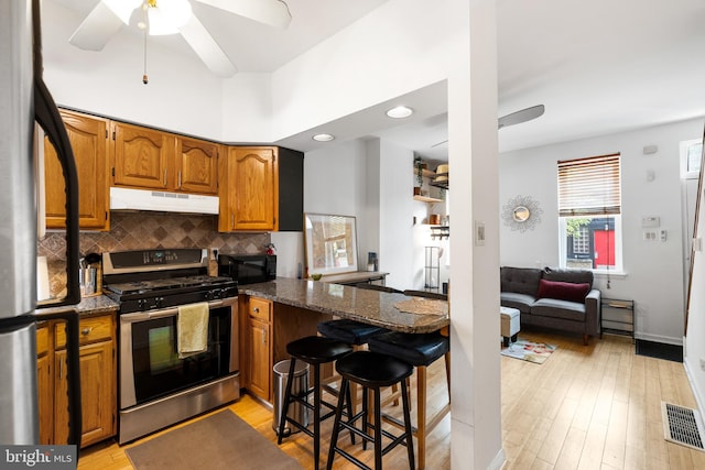 kitchen featuring appliances with stainless steel finishes, a breakfast bar, kitchen peninsula, light hardwood / wood-style flooring, and ceiling fan