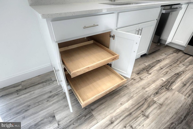 interior details featuring light hardwood / wood-style floors, sink, stainless steel dishwasher, and white cabinets