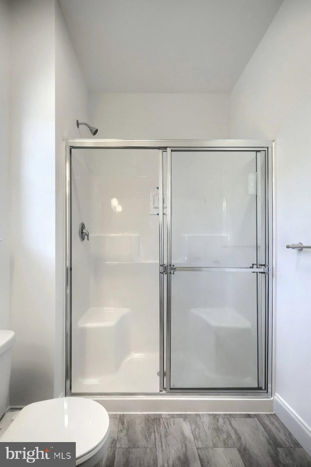 bathroom featuring hardwood / wood-style floors, a shower with shower door, and toilet