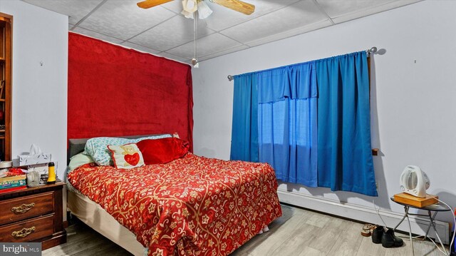 bedroom with a drop ceiling, a baseboard heating unit, ceiling fan, and light hardwood / wood-style floors