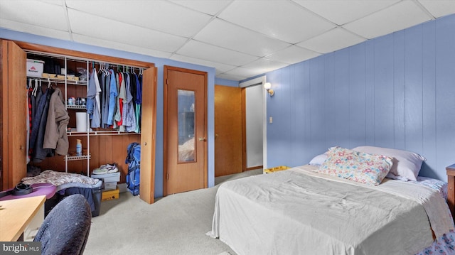 bedroom featuring a closet, light colored carpet, wooden walls, and a drop ceiling