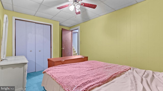 bedroom featuring light colored carpet, ceiling fan, a closet, and a drop ceiling