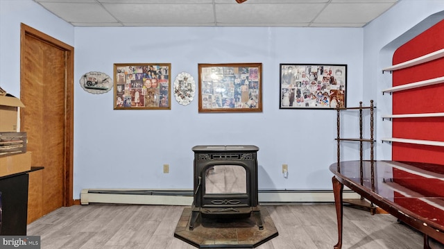 interior space featuring a baseboard radiator, a wood stove, light hardwood / wood-style floors, and a drop ceiling