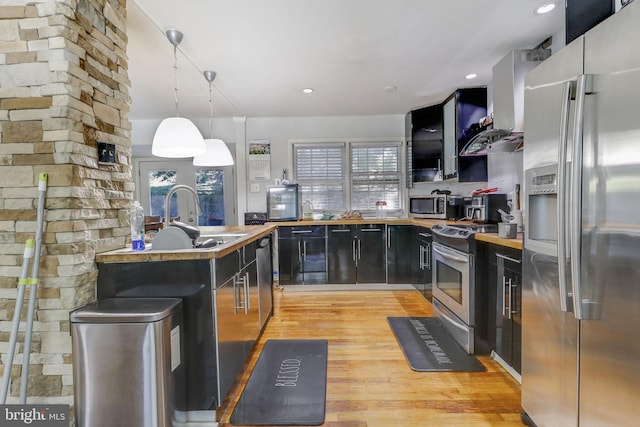 kitchen featuring light wood-type flooring, stainless steel appliances, sink, hanging light fixtures, and wall chimney range hood