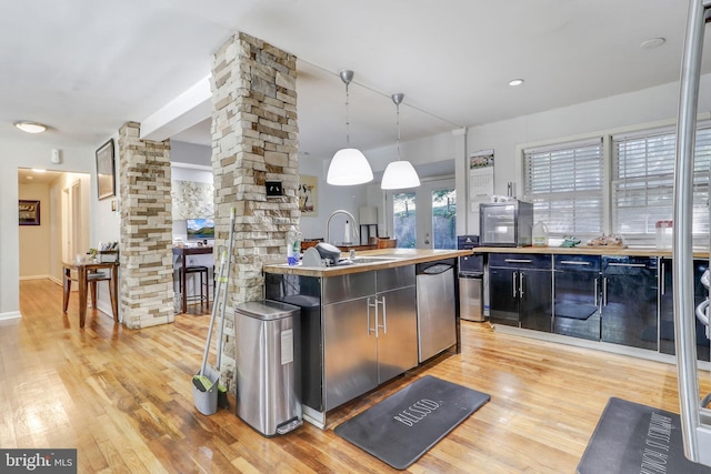 kitchen featuring light wood-type flooring, sink, an island with sink, and decorative columns