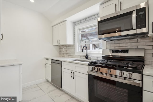 kitchen with baseboards, lofted ceiling, appliances with stainless steel finishes, marble finish floor, and backsplash